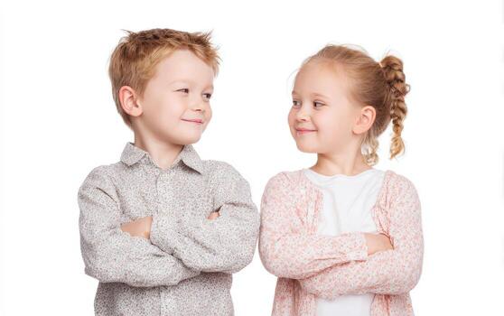 Two children, a boy and a girl, standing side by side with arms crossed, smiling at each other, showcasing playful interaction and friendship in a bright, cheerful atmosphere photo