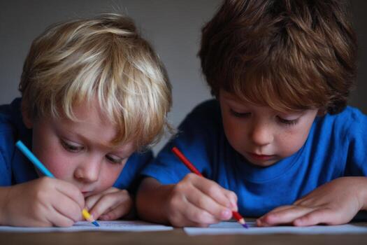 Two young boys engaged in creative drawing activity, using colorful crayons on paper, showcasing concentration and artistic expression in a cozy indoor environment photo