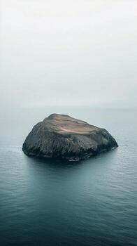 Remote island surrounded by calm waters under overcast sky at twilight photo