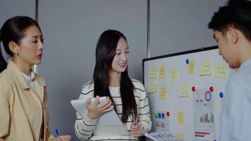 grupo de asiático compañeros de trabajo en pie en frente de un blanco tablero con gráficos y cuadro, analizando corporativo estrategia, revisando plan, gerente financiero proyecto visión de conjunto a oficina reunión, lluvia de ideas. video