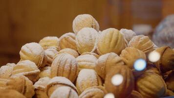 valnöt formad småkakor täckt i pulveriserad socker, visas under festlig lampor i en bageri fönster video