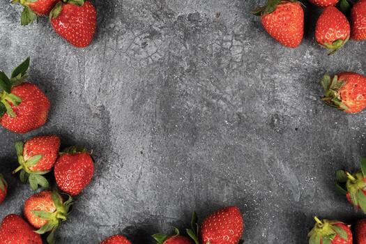 Fresh red strawberries frame the edges of a dark gray concrete texture background with ample copy space. photo