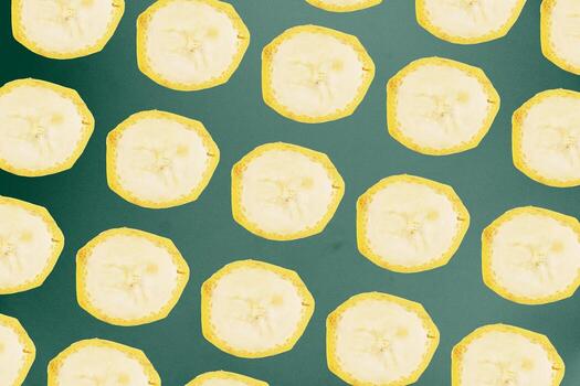 Round cut banana slices form a repeating grid pattern against a dark green background surface. photo