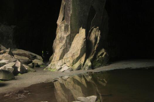 A man standing in front of a cave with a large rock photo