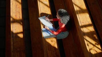 topp se från ovan kvinna flicka studerande kvinna studie på tabell skrivning studerar inlärning skriva lära sig kurs häfte i tömma solig skuggor klass högskola universitet hörsal ser på kamera leende video