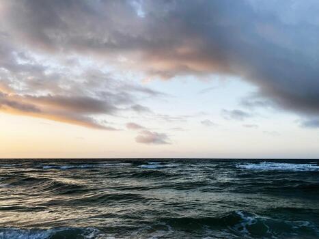Sunset over calm Florida coast with waves under dramatic clouds in open sea at dusk photo