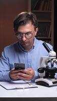 vertical cientista usando Smartphone dentro laboratório com microscópio e livros video