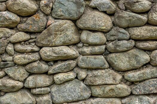 Rustic stone wall showcases various stones arranged in unique shapes and sizes. Weathered texture adds character to this outdoor scene with a tranquil mood. photo