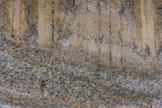 Close-up shot of a textured concrete wall showing signs of weathering and the embedded aggregate material. Vertical stains run down the upper portion of the wall. photo