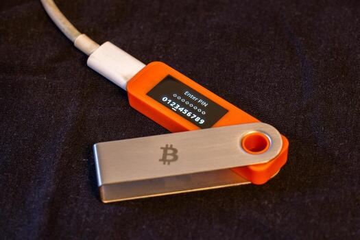 Hardware security device shows PIN entry prompt with Bitcoin logo. Set on dark fabric, this image conveys a sense of technological security during daytime. photo