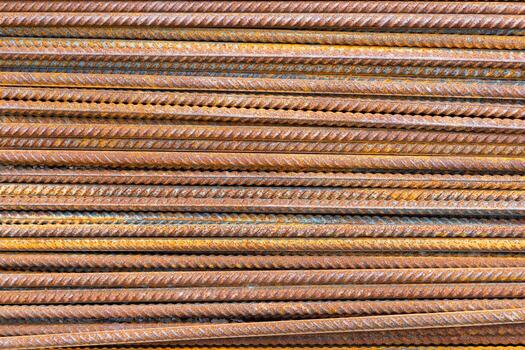 Many rusty metal rebar rods are arranged in parallel at an outdoor construction site. The weathered texture and industrial setting create a rustic and raw atmosphere during the day. photo