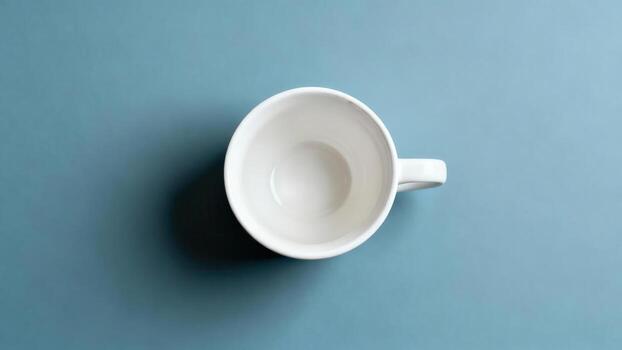 Plain white ceramic drinking vessel sits centered against a muted blue background viewed from above photo