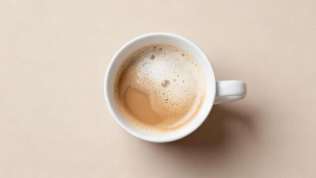 White ceramic mug filled with frothy hot beverage rests on a smooth, light surface seen from above photo