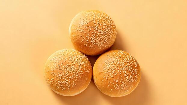 Three golden brown baked bread rolls topped with seeds are arranged on a plain warm colored surface photo