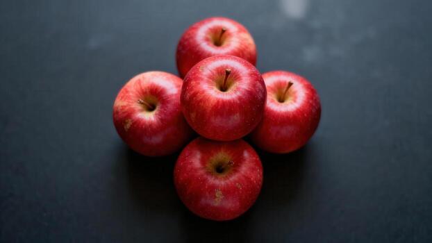 Five ripe red apples are arranged in a cross shape on a dark surface. photo