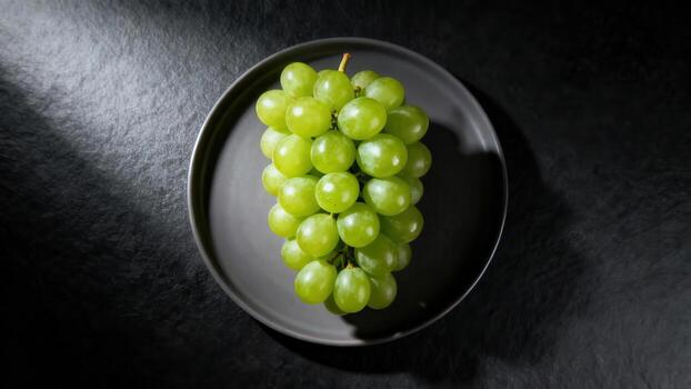 A cluster of fresh green grapes rests on a dark plate. photo