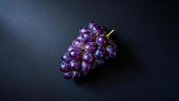 A dark purple grape cluster rests on a dark, textured surface. photo