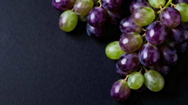 Ripe purple and green grapes rest on a dark textured surface. photo