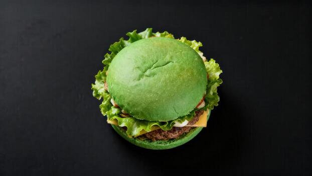 Unconventional green bun hamburger resting on a dark, plain background viewed from above photo