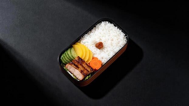 Rectangular packed meal container displays grilled meat, rice, and assorted pickled vegetables against a dark background photo