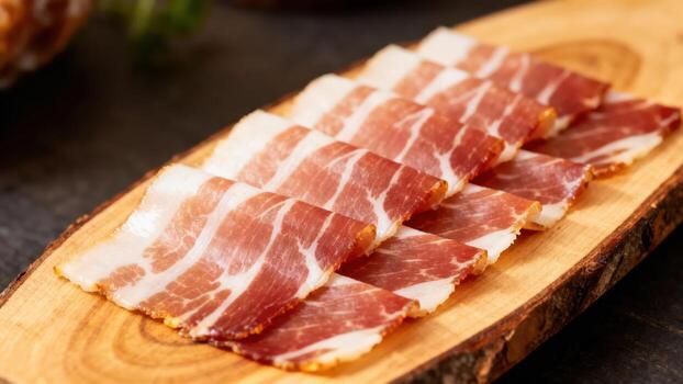 Thinly sliced cured meat displays rich marbling arranged neatly on a rustic wooden board. photo