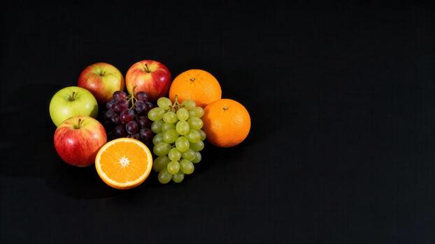 Assortment of fresh produce including apples, oranges, and grapes sits against a dark background photo