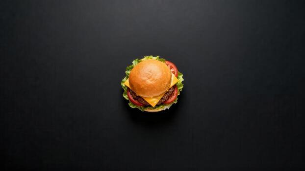 Single cheeseburger positioned centrally atop a dark, uniform background viewed from above photo