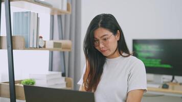 Jeune femme travail sur portable dans moderne Bureau avec étagères et ordinateur écran affichage code, concentré sur tâche avec Naturel lumière éclairant le espace video