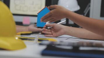 A person is holding a house model while another person is working on a computer video
