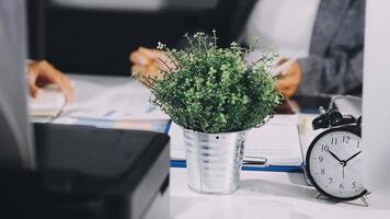 uma plantar dentro uma Panela em uma escrivaninha com uma relógio e uma computador portátil video
