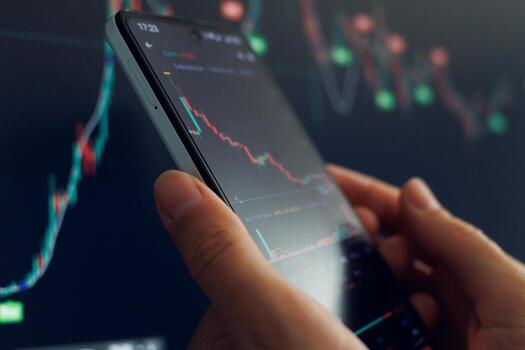 Trader utilizes smartphone to examine fluctuating stock market graphs and data trends during trading hours photo