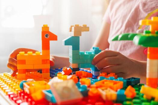 Child's hands hold colorful building block animals they created, showcasing imagination and fun with a toy constructor set in bright sunlight. photo