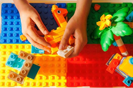Top-down view of child's hands building with colorful toy constructor blocks on a vibrant baseplate, creating shapes and structures. Hands-on creative play. photo