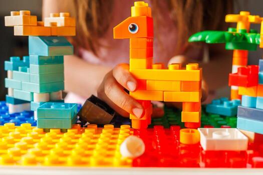 Child's hand holds a colorful building block giraffe, a result of imaginative play and creativity with a toy constructor set in bright sunlight. photo