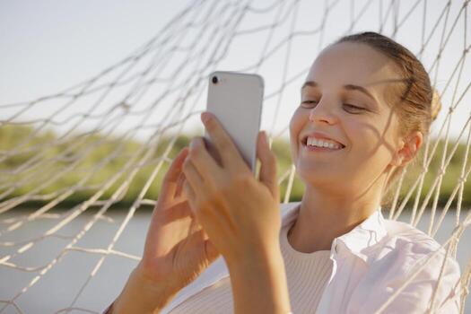 Woman smiling with smartphone in hammock photo