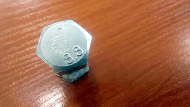 Hexagonal bolt resting on a wooden table displays detailed markings and reflections photo