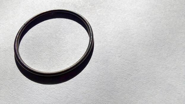 Round spring resting on smooth paper surface with gentle light casting shadow photo