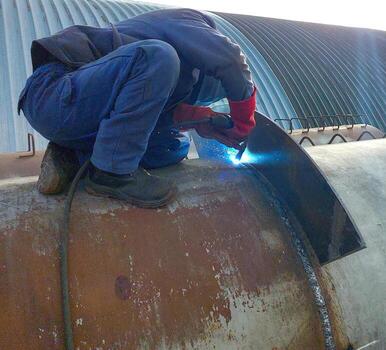 Welder performing a pipe welding task in an industrial setting during daylight hours photo