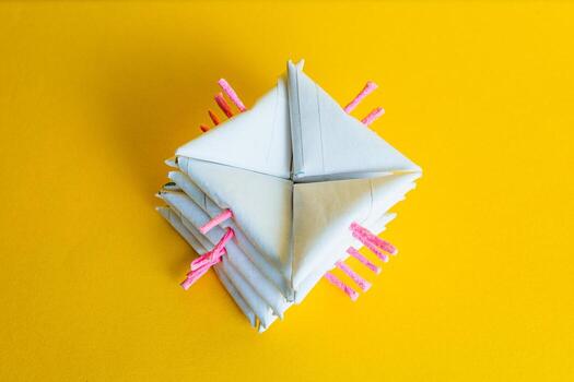Close-up of a stack of white triangular-shaped paper firecrackers, displaying the pink fuses, on a bright yellow background. photo