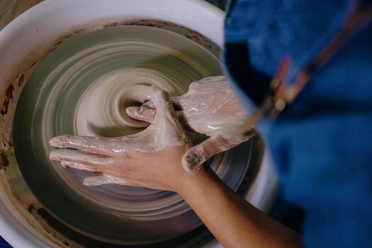 Close-up of a potter's hands shaping fresh clay on the spinning wheel, creating a ceramic object with a sense of motion photo