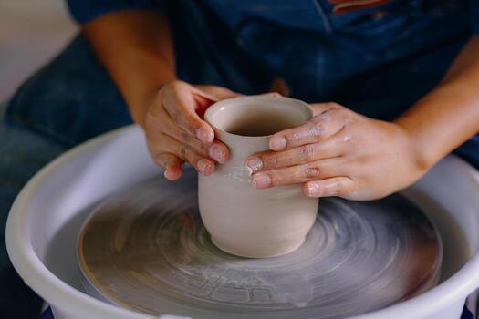 Close up of expert hands modeling and refining a tall wet clay cup spinning on the wheel in a pottery workshop photo