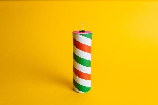 Cylindrical pyrotechnic firecracker with a red, green, and white striped design on a smooth, vibrant yellow studio background. photo
