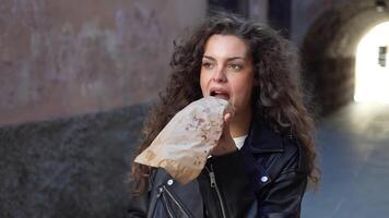 uma jovem mulher com encaracolado cabelo capturado dentro a urbano configuração enquanto desfrutando uma lanche video