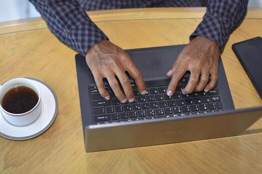 A person typing on a laptop computer with a cup of coffee photo