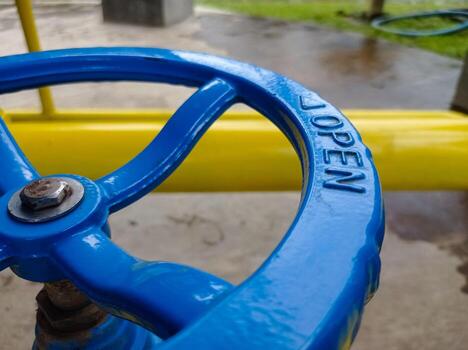 Vibrant blue industrial valve handle with 'OPEN' text, part of a utility pipeline system photo