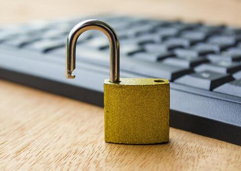 A small golden padlock standing open on a computer keyboard symbolizing cybersecurity breach, data protection risk or online account vulnerability. photo