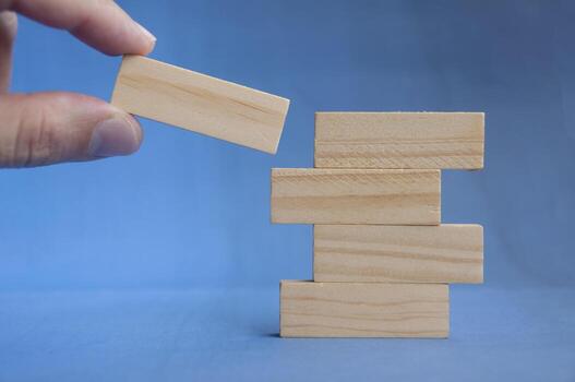 Hand preparing to place wooden block on lower stack showing teamwork and foundation concept with customizable space for text or ideas. photo