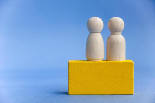 Two wooden peg figures on yellow block with blue background symbolizing teamwork. With customizable space for text or ideas photo