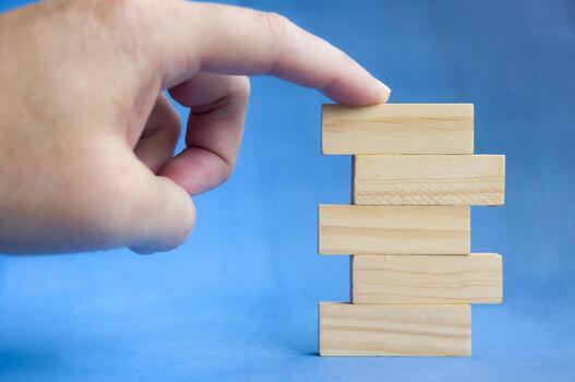 Hand holding wooden block above stacked pieces on blue background showing building and growth concept with customizable space for text or ideas. photo