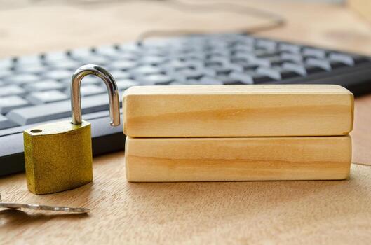 A bright brass padlock positioned on a desk near a computer keyboard with blank wooden blocks with customizable space for text. photo